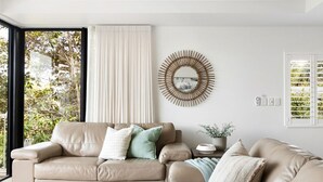 Una sala de estar moderna con un sofá de cuero color beige, un espejo redondo en la pared y vistas a zonas verdes al exterior.