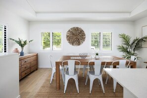 Een eetgedeelte met een houten tafel, witte stoelen en een decoratief kunstwerk aan de wand.