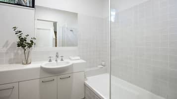 Een moderne badkamer met een wit wastafelmeubel, spiegel en bad.