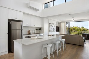 A modern kitchen with white cabinetry, a stainless steel refrigerator, and a large island with stools.
