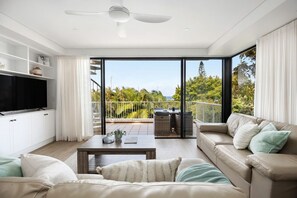 A modern living room with a flat-screen TV, a sofa, a coffee table, and a balcony with outdoor furniture.
