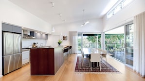 Una cocina moderna con una isla central, un comedor con mesa y sillas, y un amplio ventanal corredero que da a un espacio exterior.