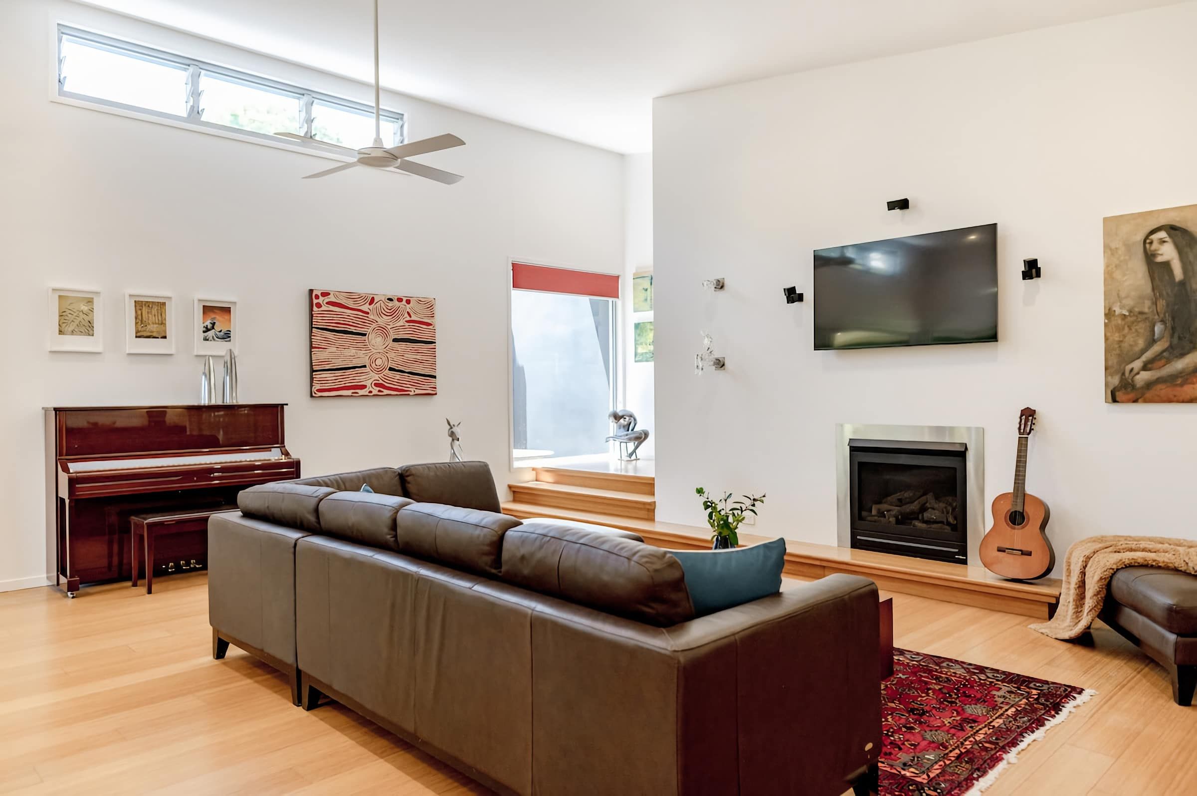 Una sala de estar amplia con un piano, un sofá modular, un televisor de pantalla plana, una chimenea y una guitarra.