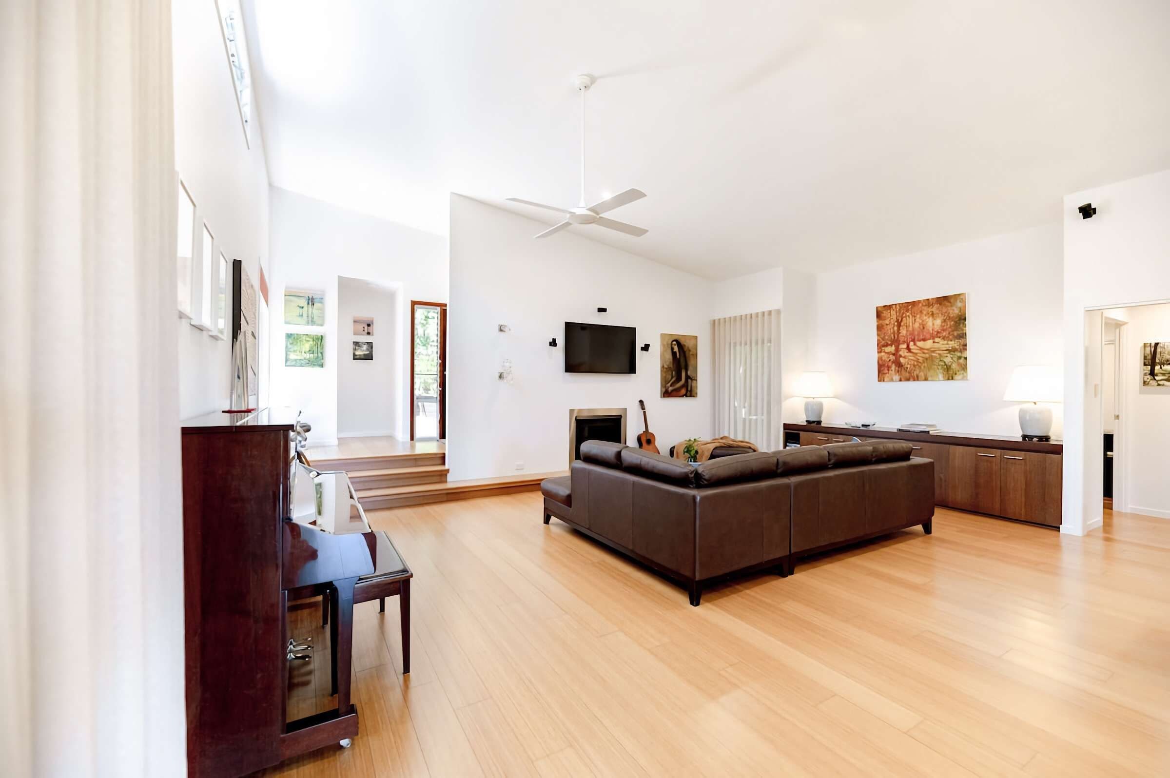 A spacious living room with a large sectional sofa, a flat-screen TV mounted on the wall, and a ceiling fan.
