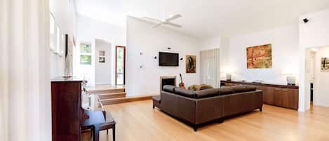 A spacious living room with a large sectional sofa, a flat-screen TV mounted on the wall, and a ceiling fan.