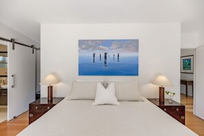 Een slaapkamer met een groot bed, twee nachtkastjes met lampen, een schilderij aan de muur en een deur naar een badkamer.