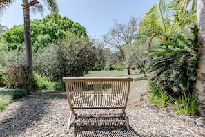 Eine hölzerne Bank in einem Garten mit Kiespflaster, umgeben von verschiedenen Pflanzen und Bäumen.