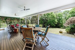 Ein überdachter Außenbereich mit Tisch und Stühlen, einem Deckenventilator und Blick auf die umliegende Natur.