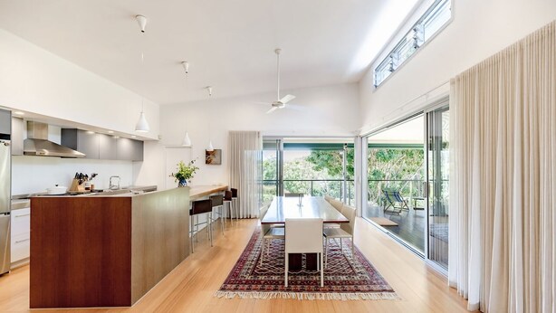 Una cocina moderna con una isla central, un área de comedor con mesa y sillas, y ventanas amplias que ofrecen vistas al exterior.
