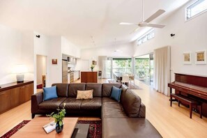 A spacious living room with a brown leather sofa, a wooden coffee table, a piano, and a ceiling fan. - Fortuna Bushland Retreat 20 min from Noosaville (Verrierdale)