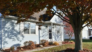 A single-story house with a front porch, a visible garage door, and a tree with autumn leaves.