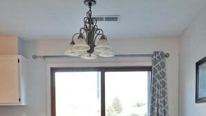 A dining area with a table and chairs, a chandelier, and a view through a large window.