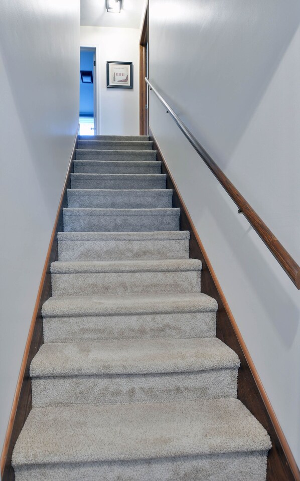 Una escalera con alfombra, barandillas de madera y una puerta al final.