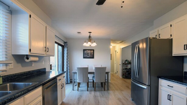 A modern kitchen with stainless steel appliances, white cabinetry, and a dining area with a chandelier.