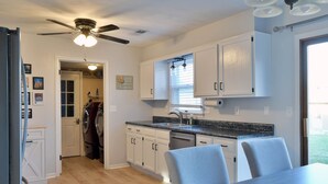 A modern kitchen with white cabinets, a granite countertop, and a ceiling fan.