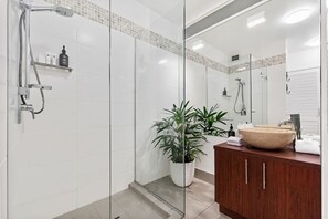 Ein modernes Badezimmer mit Duschkabine aus Glas, einem Holzwaschtisch, einem großen Spiegel und einer Zimmerpflanze.