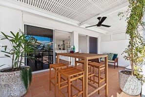 Eine Terrasse im Freien mit Holztisch und -stühlen, Blumentöpfen und einer Glastür, die in einen Innenbereich führt.