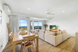 A modern living room with a wooden dining table, beige sofa, and a large TV. - 8 Andari Sunshine Luxury 1min to Beach (Sunshine Beach)
