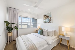 A hotel room with a bed, a window with blinds, a ceiling fan, a wall-mounted painting, a bedside table with a lamp, and a potted plant. - 8 Andari Sunshine Luxury 1min to Beach (Sunshine Beach)