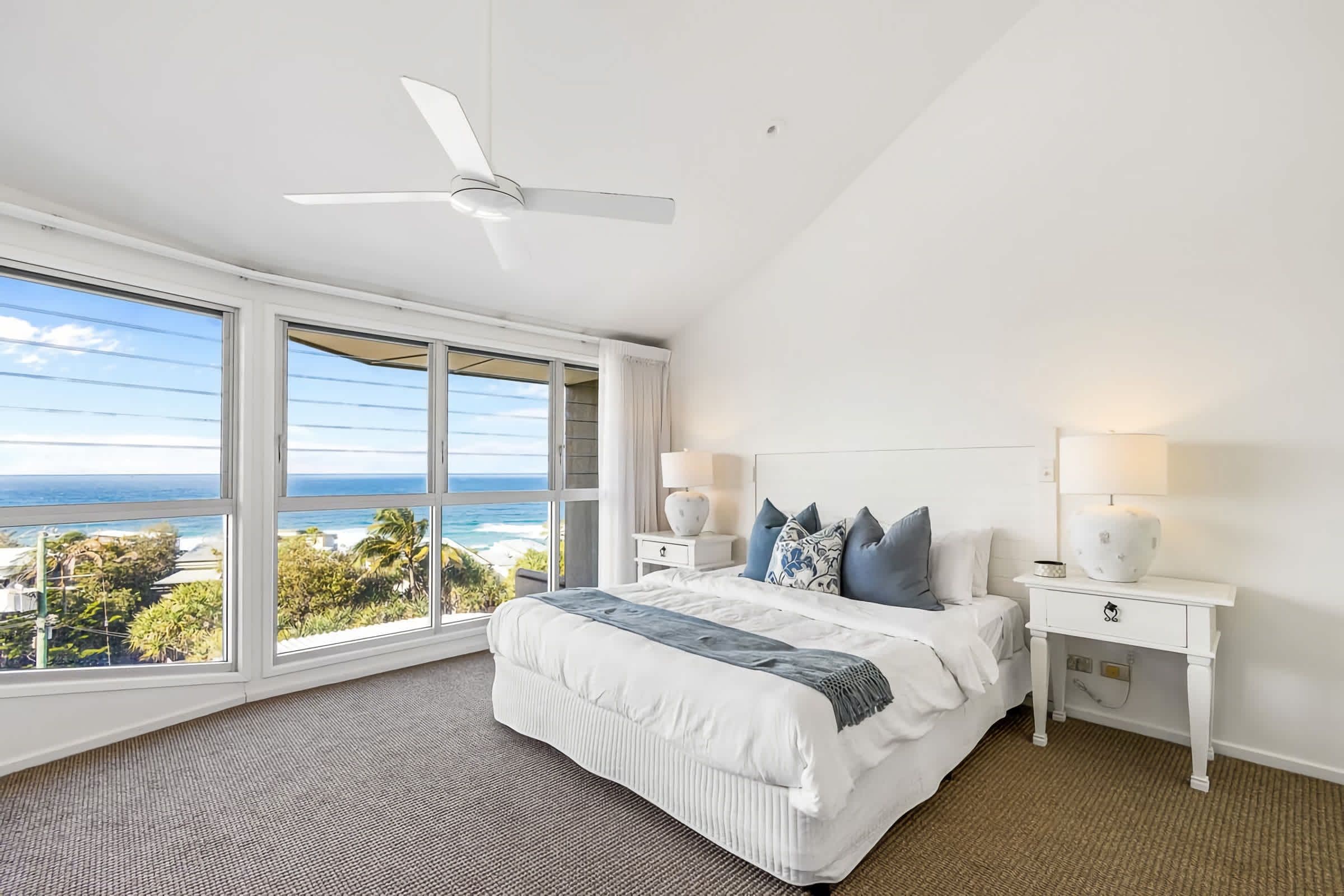 A bedroom with a large window, a ceiling fan, and a bed with pillows.