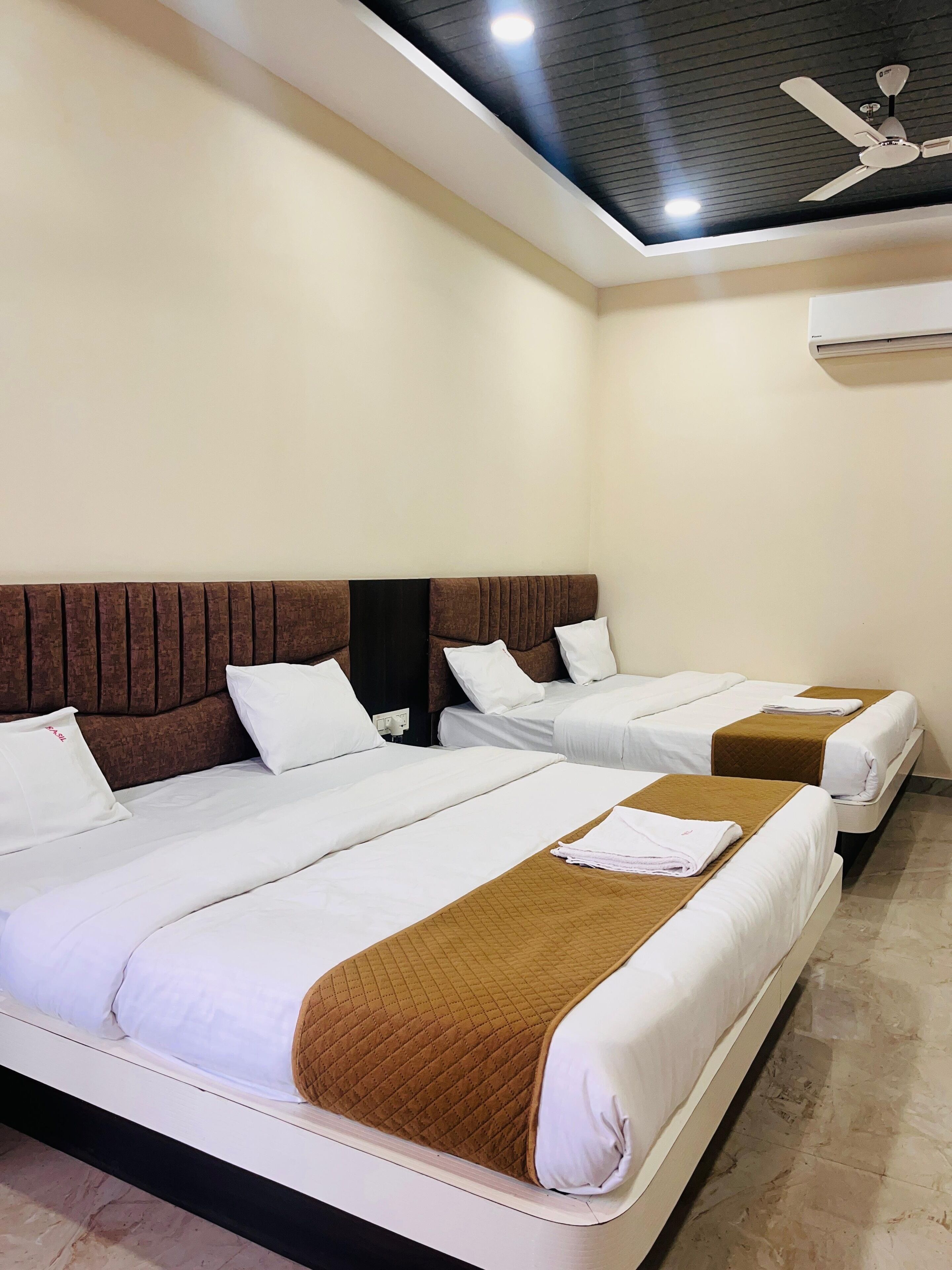 Habitación de hotel con tres camas, ventilador de techo y aire acondicionado.