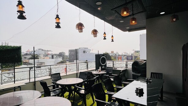An outdoor dining area with tables and chairs, a view of the city, and hanging lights. - Hotel Basil Inn (Ujjain)