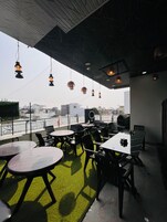 An outdoor dining area with tables and chairs, a view of the city, and hanging lights.