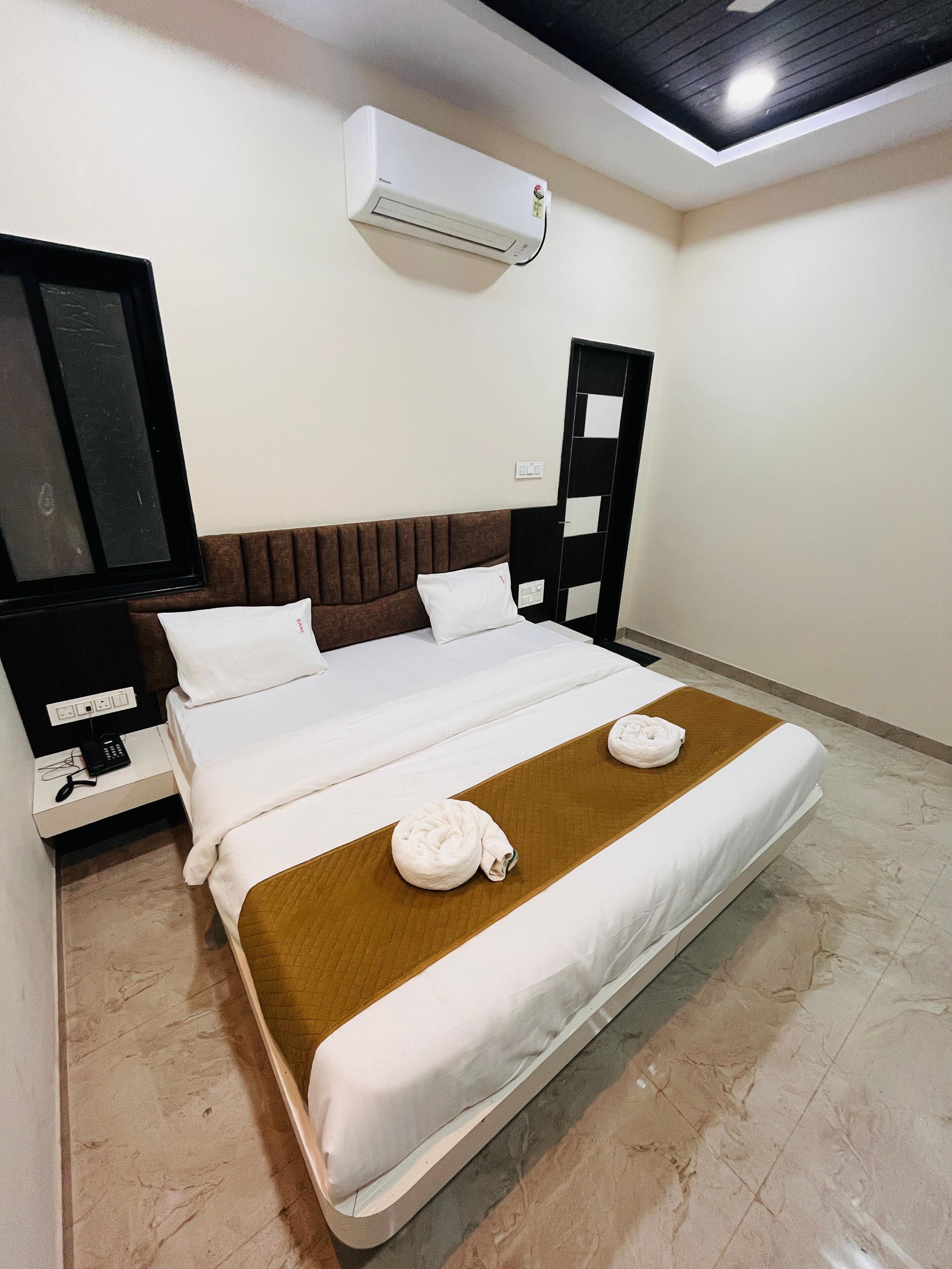 A hotel room with a bed, a TV, an air conditioner, and a bathroom door.