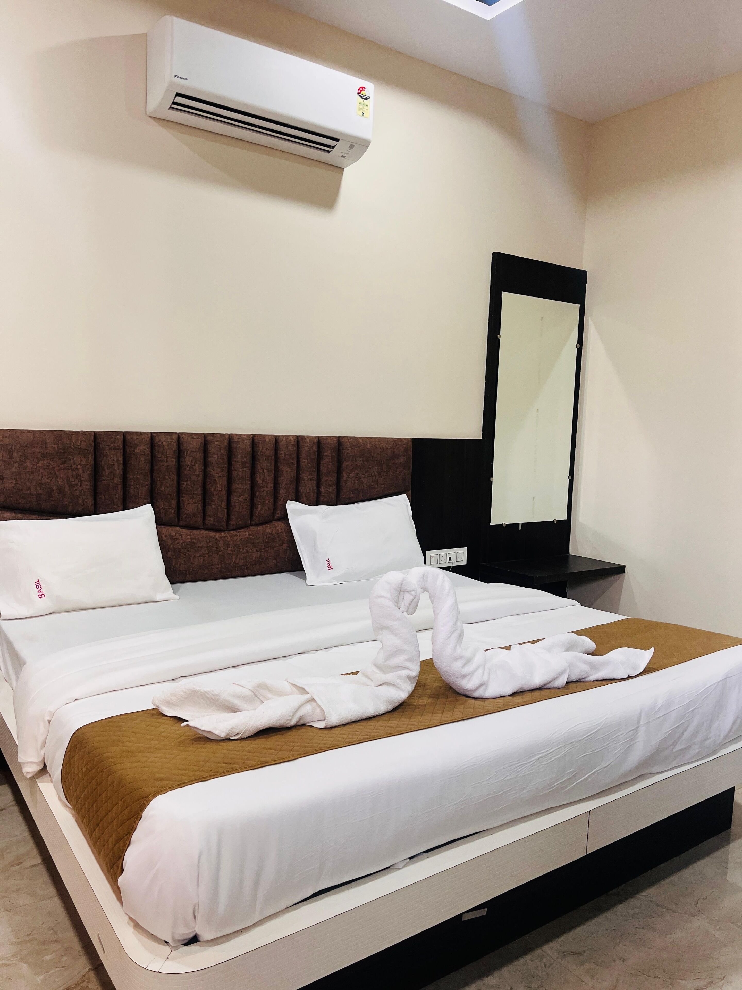 Une chambre d’hôtel avec un lit, une tête de lit marron, un oreiller blanc, une couverture blanche et une serviette pliée sur le lit.
