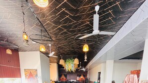 A long dining table with a plaid tablecloth, surrounded by black chairs, in a room with a high ceiling and hanging lights. - Hotel Basil Inn (Ujjain)
