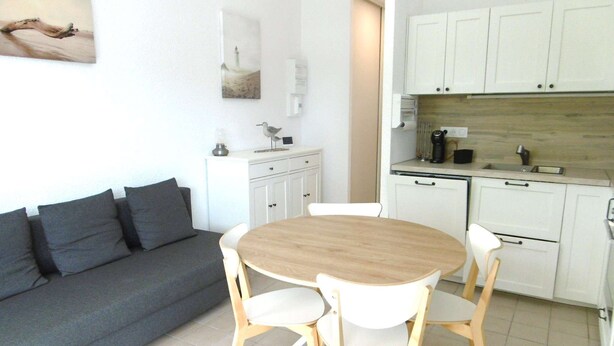 Een moderne keuken met witte kasten, een houten eettafel met vier stoelen, en een grijze bank met kussens.