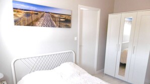Een slaapkamer met een bed, een kledingkast, een nachtkastje en een schilderij aan de muur.
