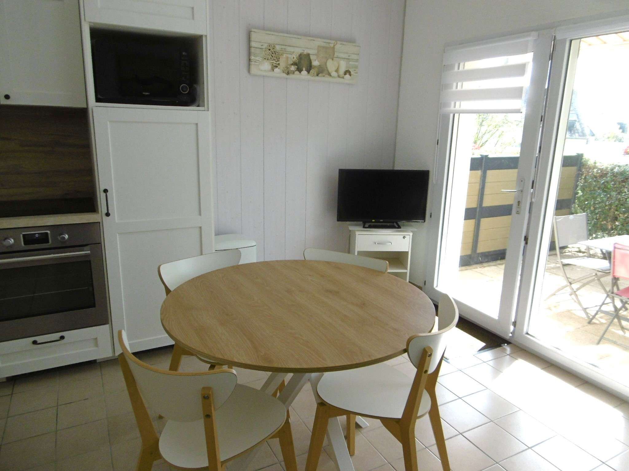 A kitchen with a microwave, oven, and a dining table with chairs. There's a television on a stand and a sliding glass door leading to an outdoor area.