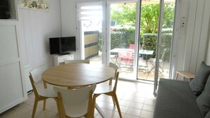 Een eethoek met een ronde tafel, stoelen, een televisie en een schuifdeur die leidt naar een terras.