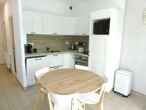 A compact kitchen with white cabinets, a microwave, a sink, and a small dining table with chairs. - 4 person beachfront apartment in seaside resort (DAMGAN)