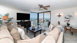 Un salon avec un canapé, une table basse et un téléviseur. Il y a un balcon avec vue sur l’océan.