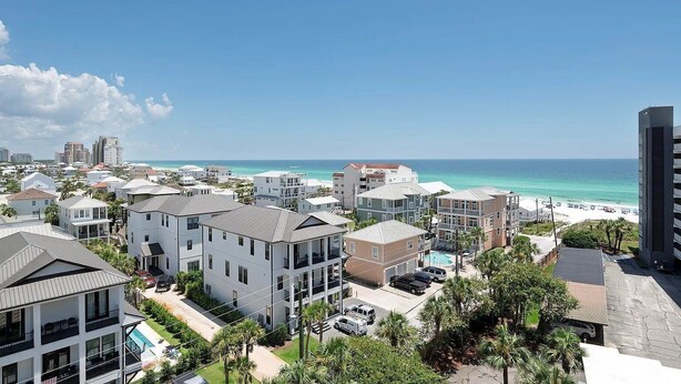 Un quartier résidentiel situé sur la côte, avec des immeubles à plusieurs étages, une piscine bien visible et une plage en arrière-plan.