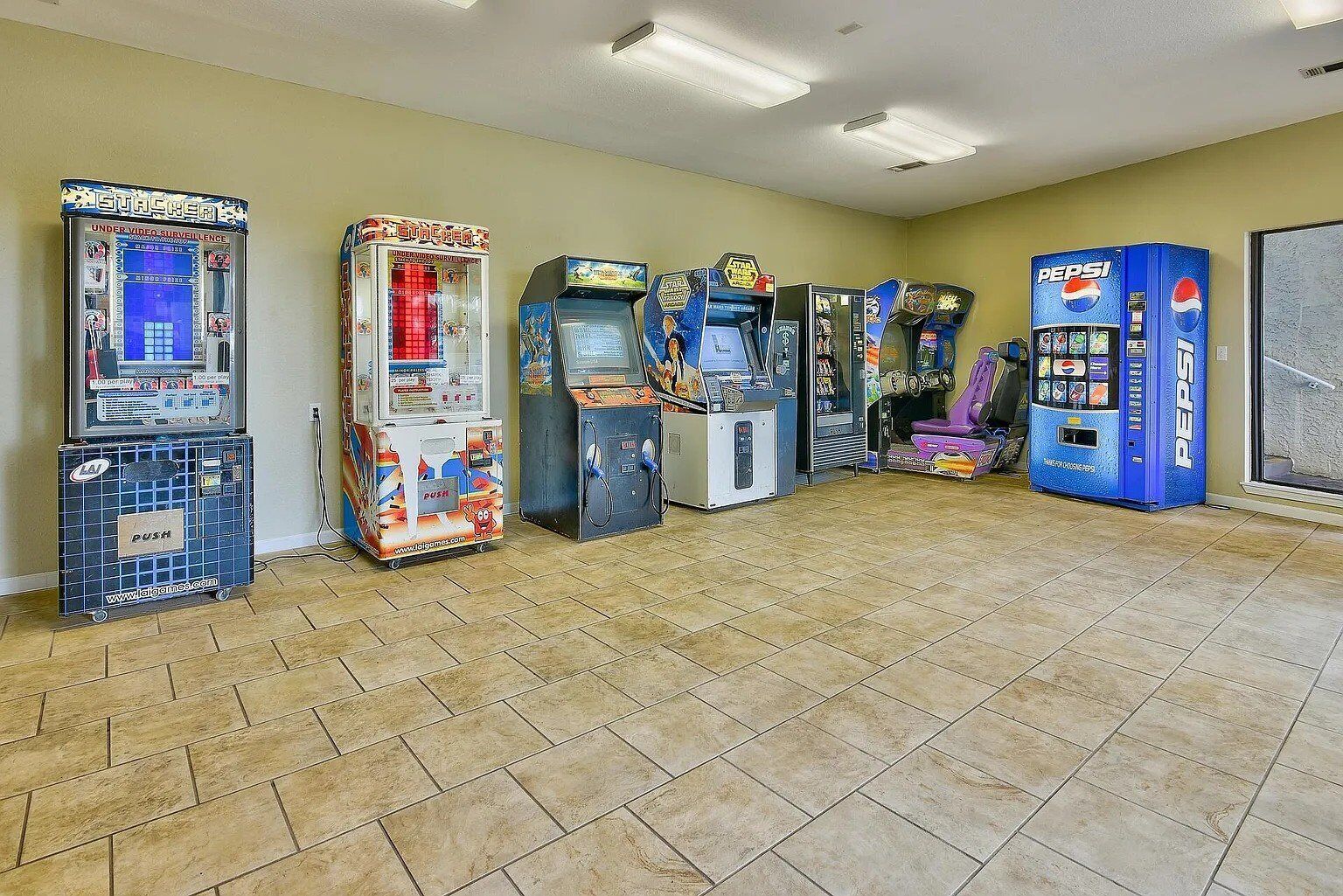 A row of arcade machines in a room with tiled flooring and beige walls.