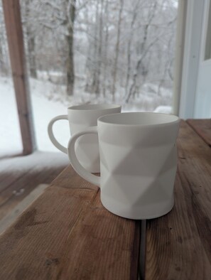 Deux tasses en céramique blanche sont posées sur une table en bois, et par la fenêtre, on aperçoit un paysage enneigé.