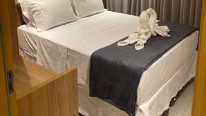 Een hotelkamer met een bed, een donkere plaids en een set witte handdoeken op het bed.