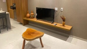 Een moderne woonkamer met een houten tv-meubel, een flatscreen televisie, een houten bankje en een vaas met gedroogde bloemen.