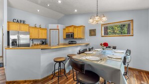 A kitchen with wooden cabinets, a stainless steel refrigerator, a microwave, and a dining area with a table set for four. - Clean comfortable home in quiet neighborhood (McCall)