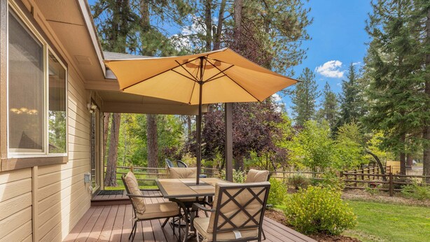 A deck with a table and chairs, a large umbrella, and a view of a wooded area. - Clean comfortable home in quiet neighborhood (McCall)