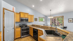 A kitchen with wooden cabinets, stainless steel appliances, a granite countertop, and a window with a view of greenery. - Clean comfortable home in quiet neighborhood (McCall)