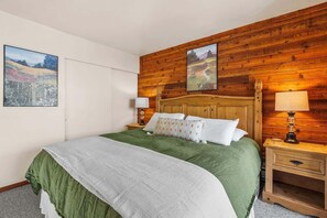 Ein Schlafzimmer mit hölzernem Kopfteil, einem Bett mit grün-weißer Bettwäsche, zwei Nachttischen mit Lampen sowie zwei Bildern an der Wand.