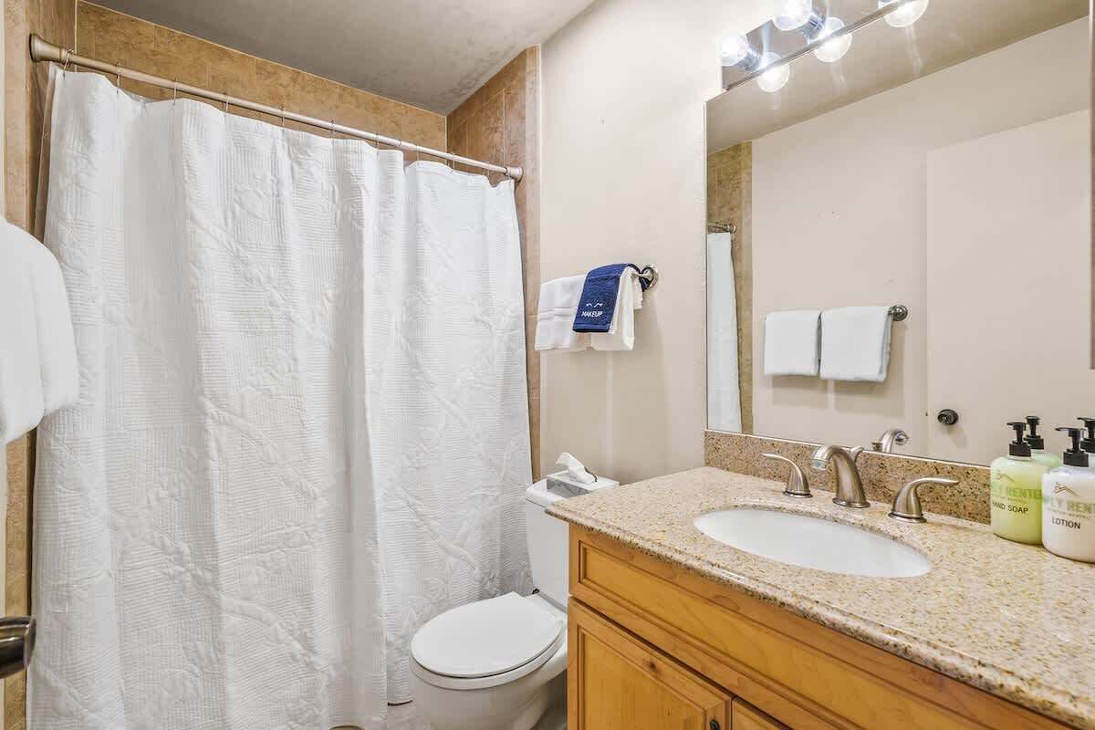 A bathroom with a shower curtain, toilet, sink, and mirror.
