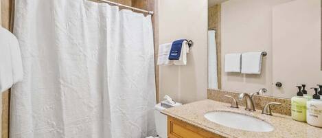 A bathroom with a shower curtain, toilet, sink, and mirror.