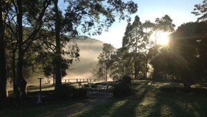 A serene outdoor setting with a pathway leading through a grassy area, surrounded by trees and a distant mountain. - Quiet Rural Retreat - Kimbriki (Mount George)