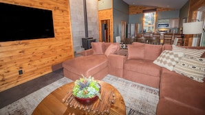 Una sala de estar acogedora con chimenea, televisor y comedor, con una cocina al fondo.