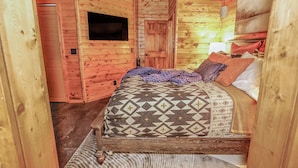 Una habitación de cabaña de madera con una cama, un televisor montado y una puerta.